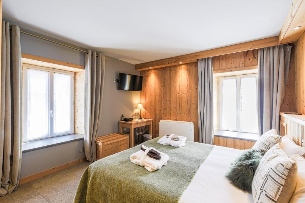 Habitación de hotel con cama, escritorio, silla, televisión y dos ventanas con cortinas.