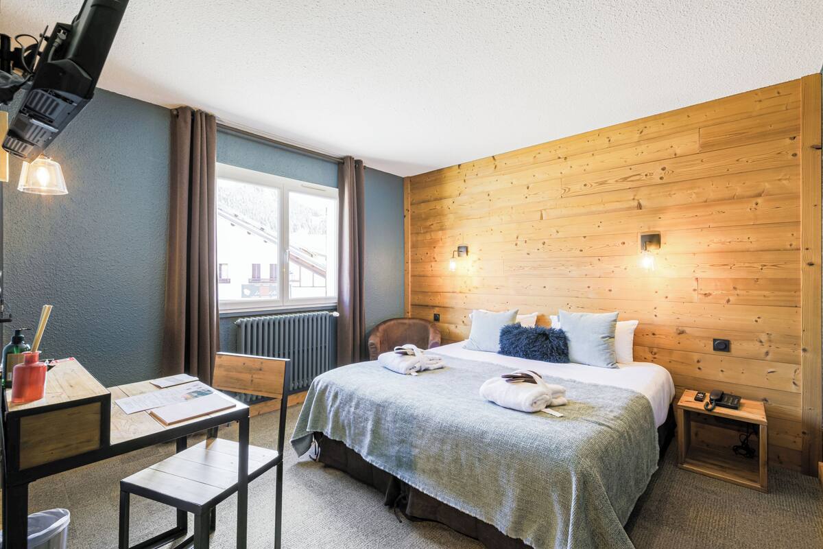 Une chambre d’hôtel avec un mur en bois, un lit avec des oreillers, une table de chevet avec une lampe, une chaise et un bureau avec une lampe.