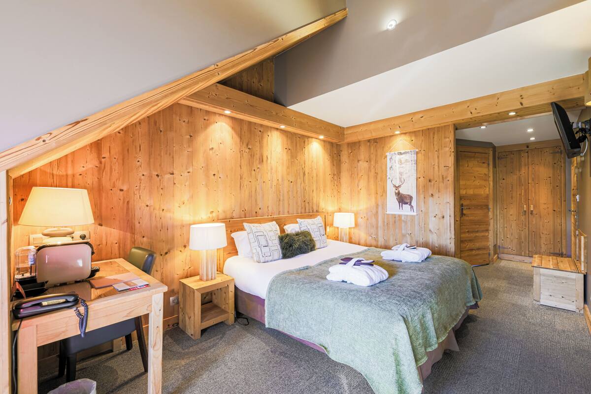 Une pièce aux murs lambrissés, comprenant un lit, un bureau et une chaise, et équipée de lampes et d’un téléphone.
