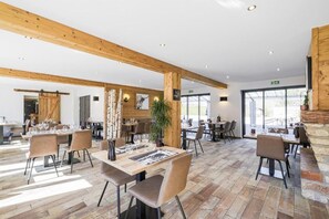 A restaurant with wooden beams, tables, chairs, and a large window.