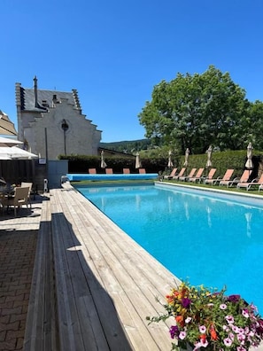 A swimming pool with a wooden deck, lounge chairs, and a castle-like building in the background.