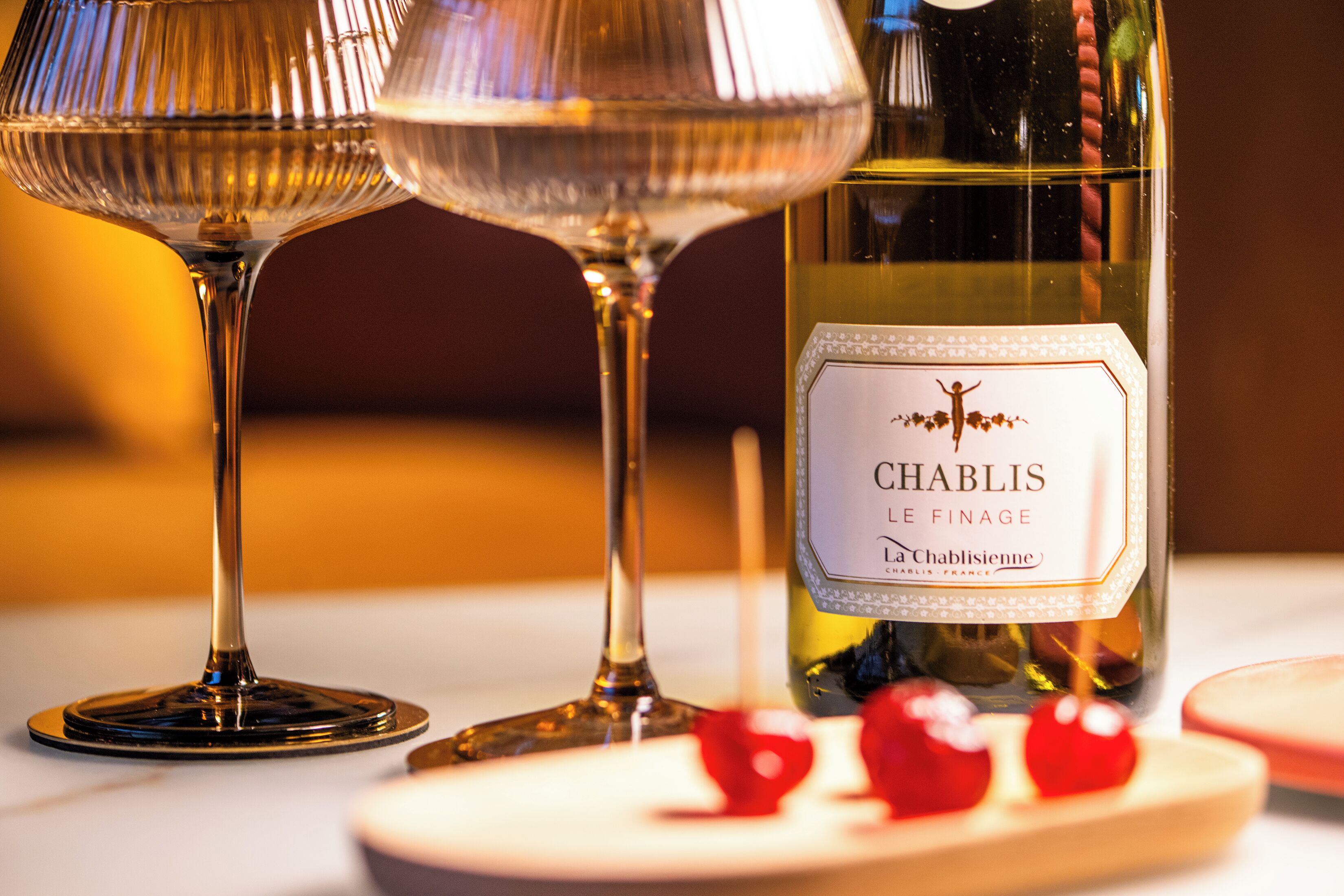Una botella de vino Chablis, dos copas de vino y un plato con cerezas.