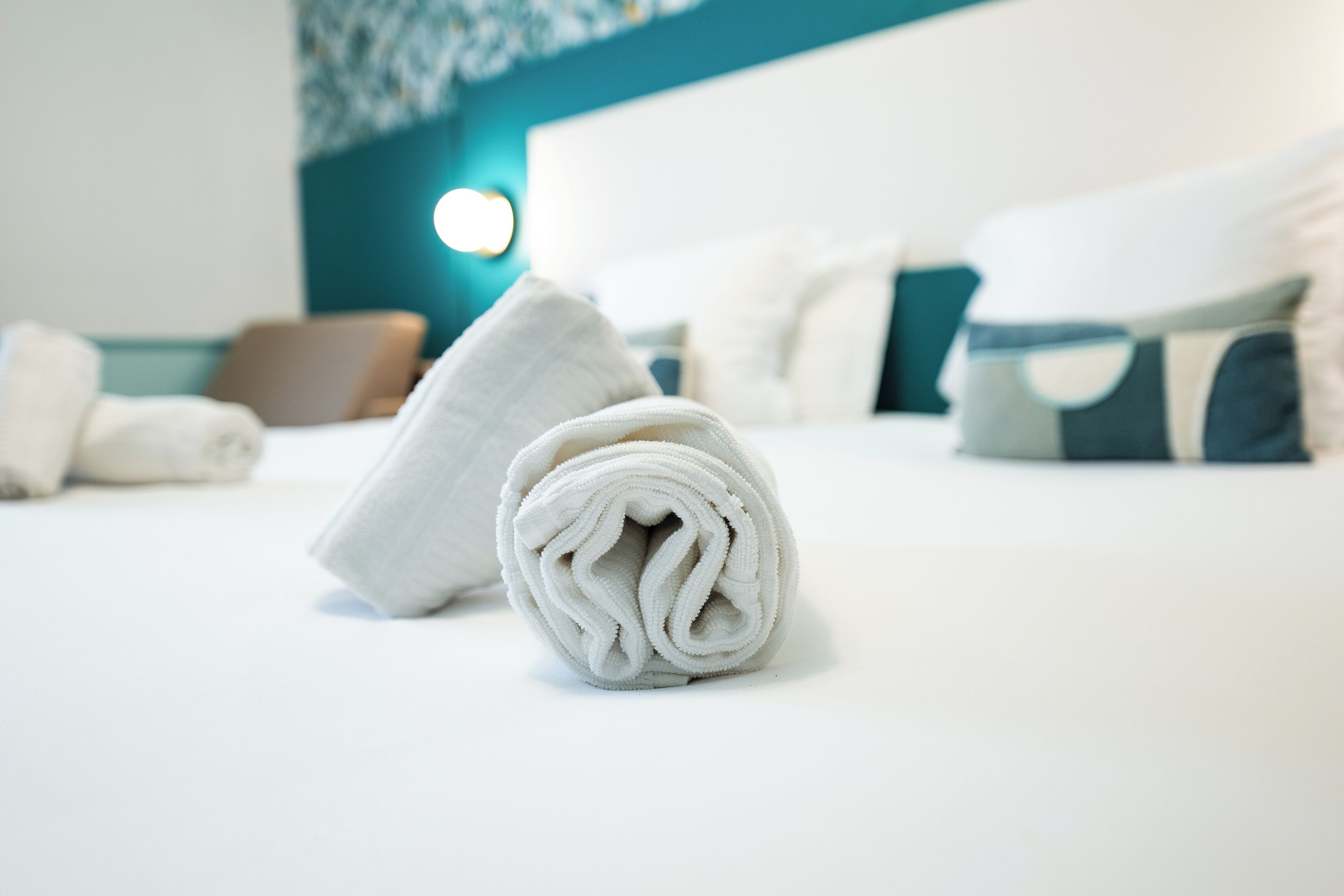 A neatly made bed with white linens and a rolled towel in the foreground.