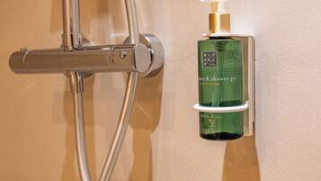 Chuveiro com chuveiro manual e frasco de shampoo e gel de banho fixado na parede.