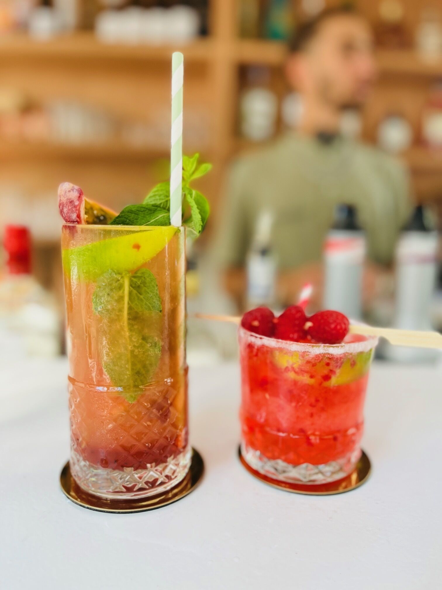 Zwei Cocktails in Gläsern mit Eis, garniert mit Minzblättern und Beeren.