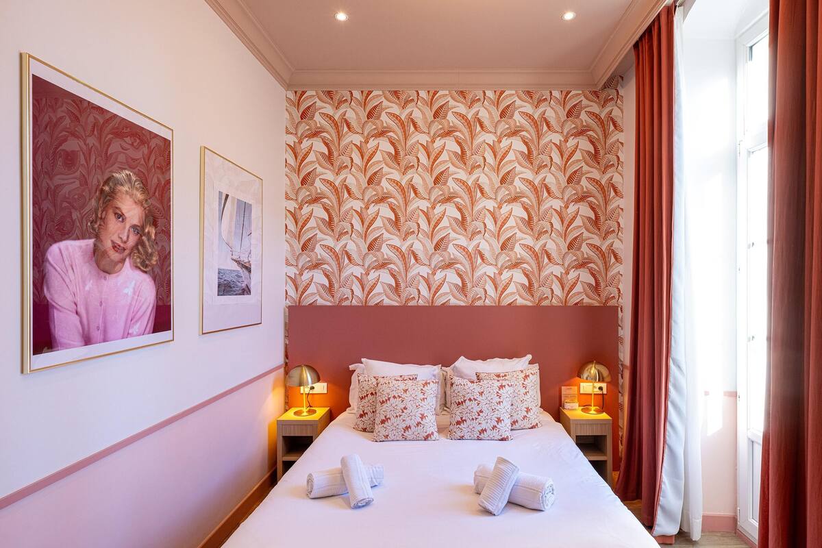 A hotel room with a large bed, two bedside tables with lamps, a floral wallpaper, and a framed picture on the wall.