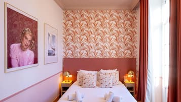 A hotel room with a large bed, two bedside tables with lamps, a floral wallpaper, and a framed picture on the wall.