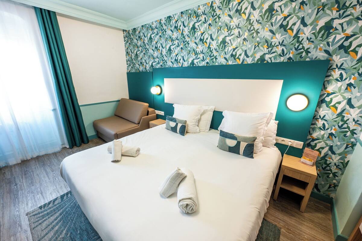 A hotel room with a large bed, two bedside tables, a sofa, and a patterned wall.