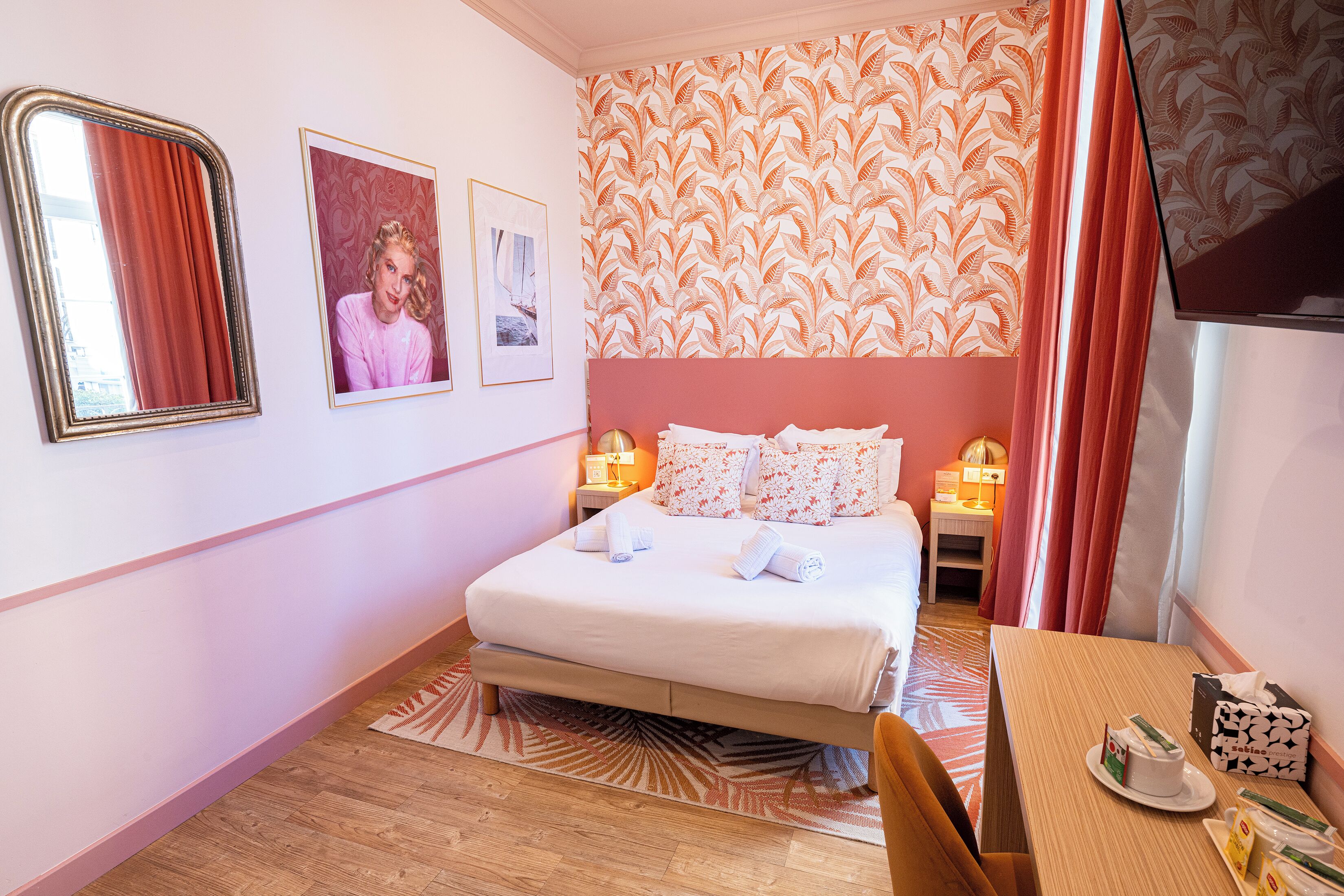 Een hotelkamer met een bed, een bureau, een spiegel en een wand met behang.