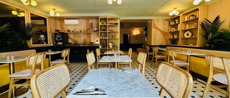 Un restaurante con un área central de comedor que presenta una mesa de mármol y sillas de mimbre, rodeado de estantes con diversos artículos.