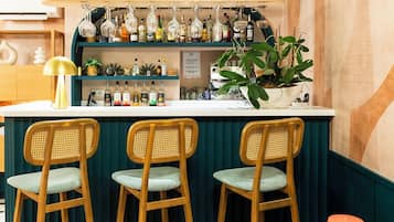 Angolo bar con tre sgabelli di legno, un bancone e assortimento di bottiglie e bicchieri.