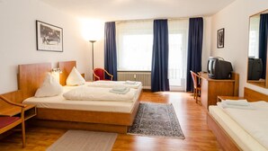 Et hotelværelse med to senge, et skrivebord, en stol, et fjernsyn og et vindue med gardiner.
