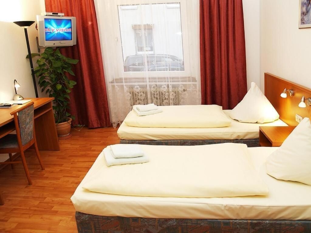 Egy kétágyas szoba, íróasztallal, televízióval és függönnyel ellátott ablakkal.