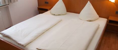 A neatly made bed with two pillows and a folded blanket, wooden headboard, bedside tables, and wall-mounted lamps.