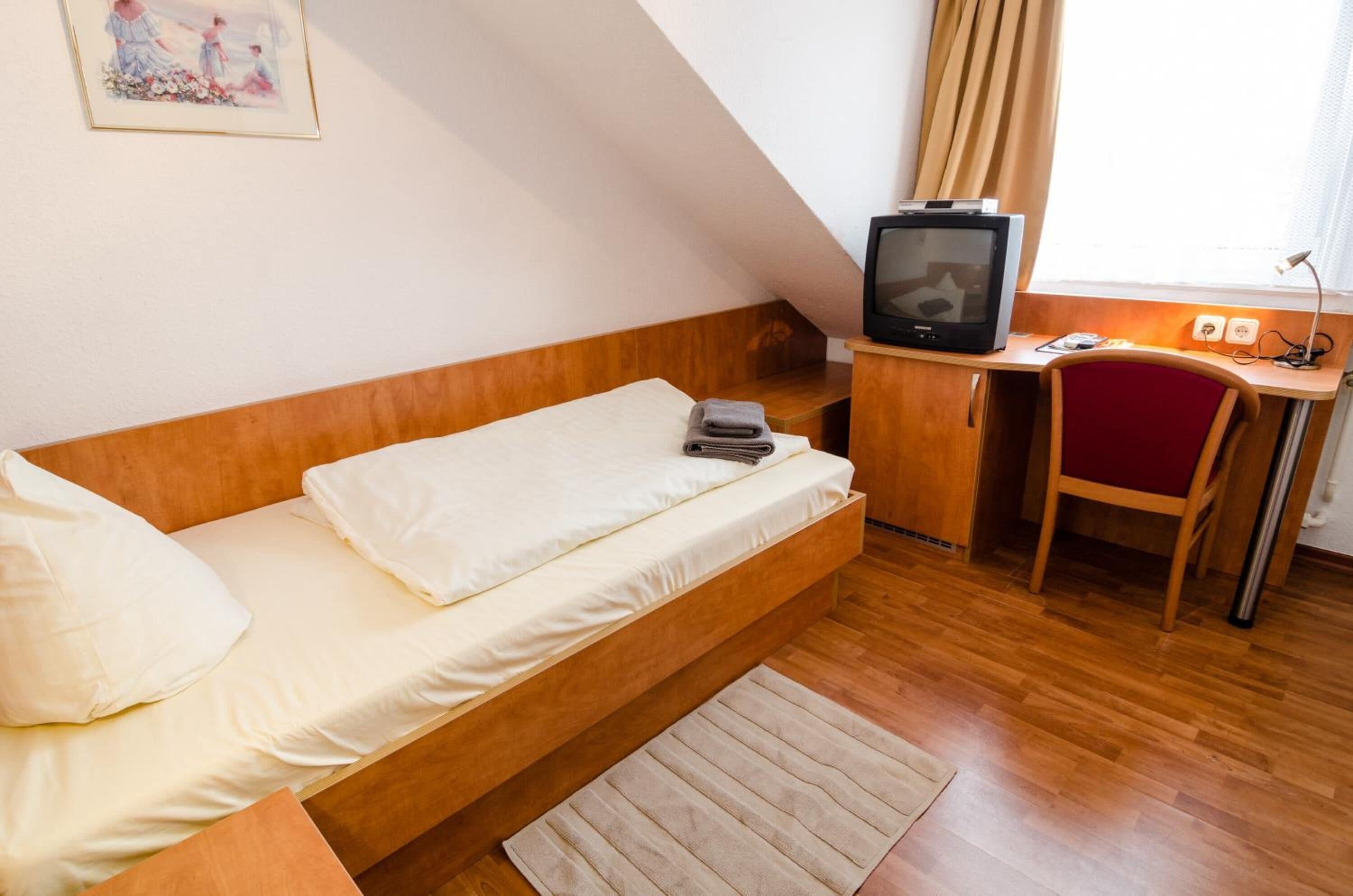 Habitación pequeña con una cama, un escritorio con computadora, una silla y un televisor.