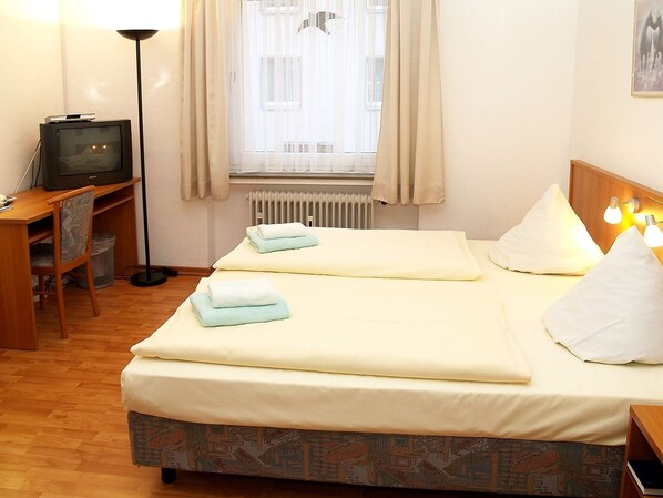 A hotel room with two beds, a desk with a television, and a radiator. - Altstadthotel Wienecke (Braunschweig)