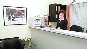 En receptionsdisk med et indrammet billede, en sort stol og en potteplante.