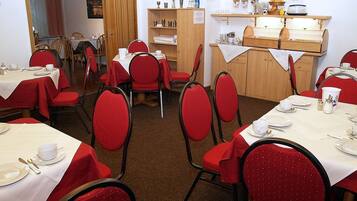 A dining area with tables set for meals, red upholstered chairs, and a buffet counter with various food items.