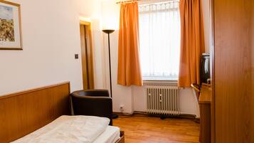 Een hotelkamer met een bed, een stoel, een bureau, een radiator en een raam met gordijnen.