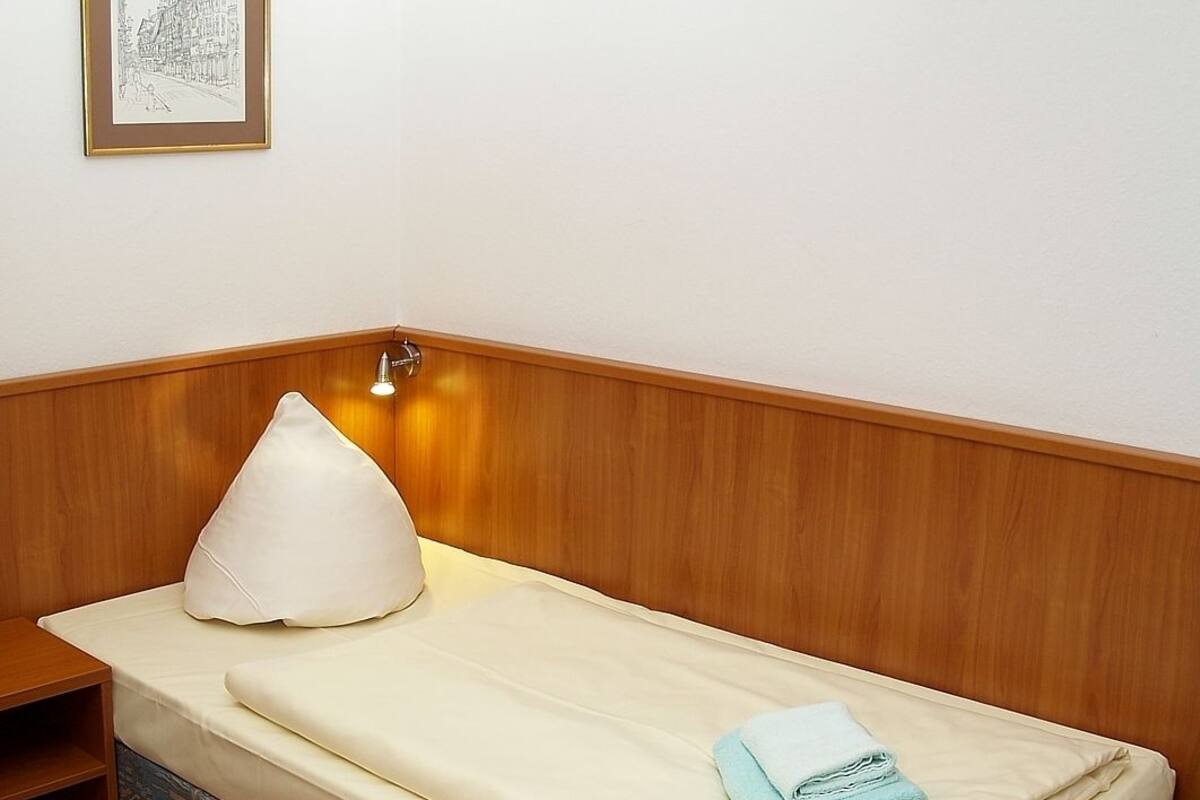 A single bed with a wooden headboard, a bedside lamp, and a framed drawing on the wall.