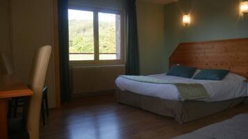 Een slaapkamer met een houten hoofdbord, een bed met wit beddengoed en teal kussens, een raam met gordijnen, en een radiator.