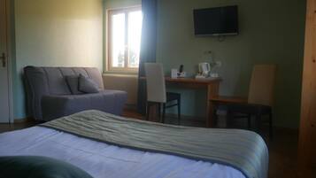 Habitación de hotel con cama, sofá, escritorio con silla, televisor y ventana con cortinas.