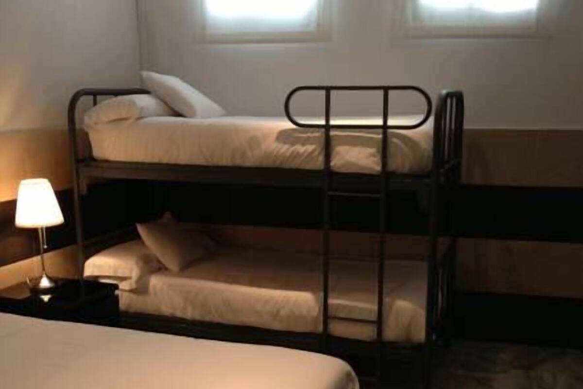 A room with bunk beds, a bedside table with a lamp, and a window with curtains.