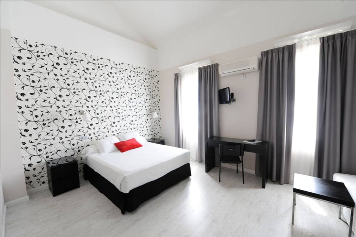 A hotel room with a bed, a desk, a chair, and a TV on the wall.