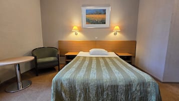 Habitació d'hotel amb un llit, una cadira, una taula petita, dues làmpades penjades a la paret i una fotografia amb marc.