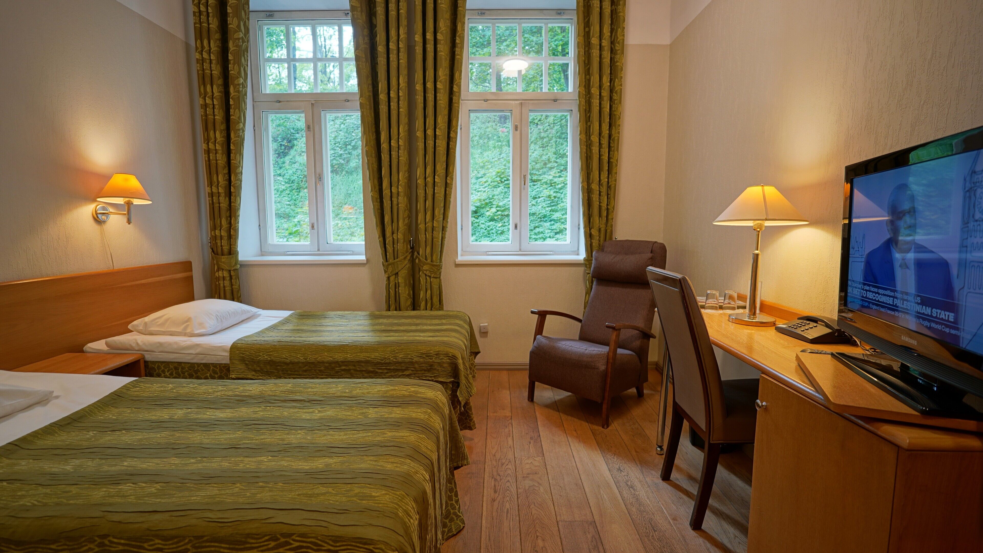 A hotel room with two beds, a desk with a television, a chair, and a window with curtains.