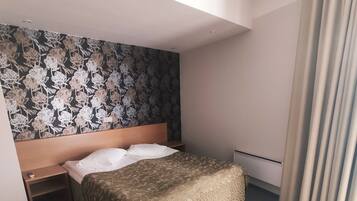 A hotel room with a bed, a headboard, a nightstand, a wall with a floral pattern, and a window with curtains.