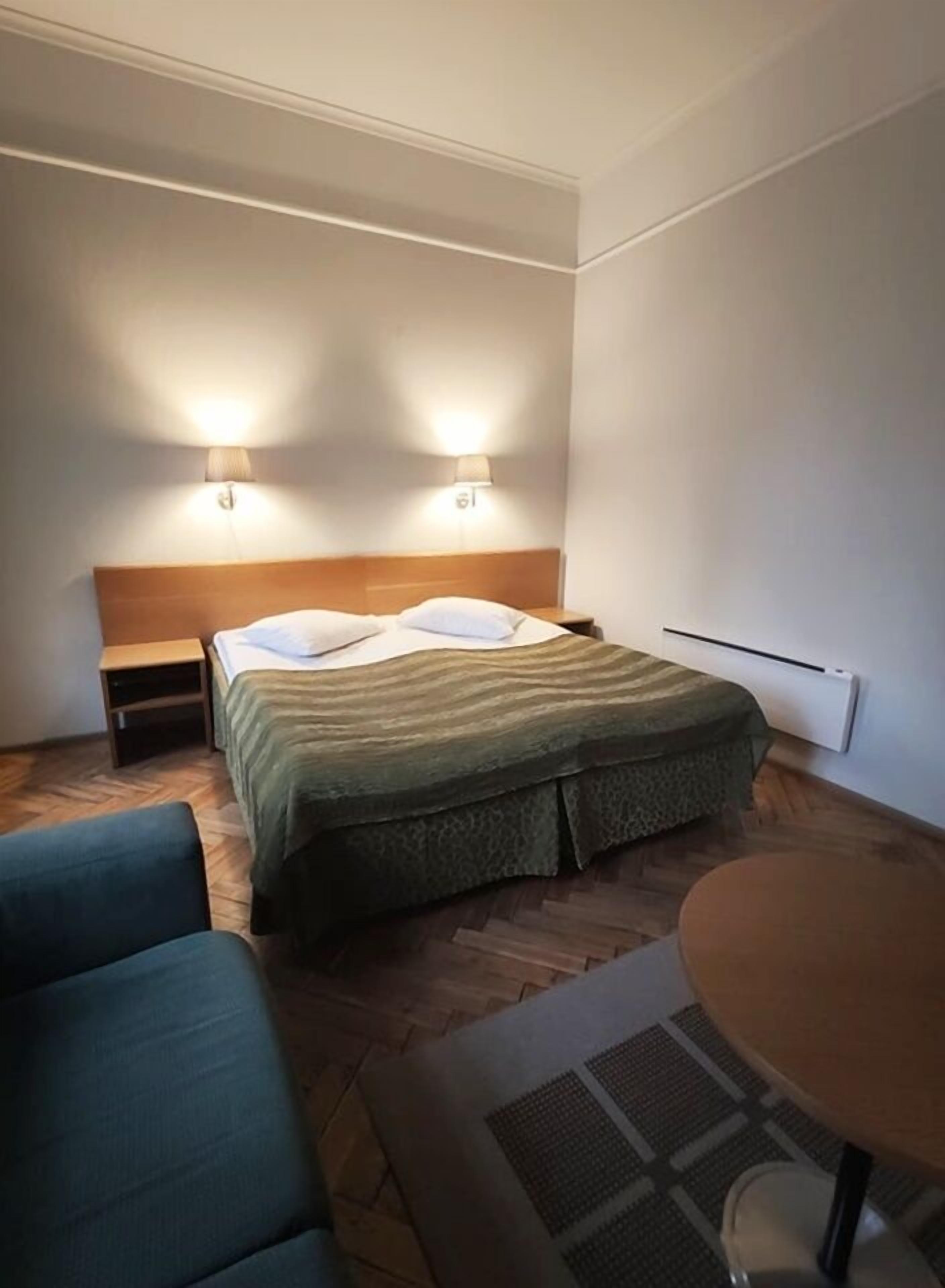 A hotel room with a bed, two bedside lamps, a small table, and a chair.