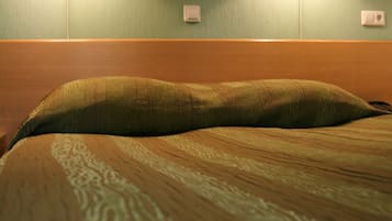 Una cama con cabecera, dos lámparas fijadas a la pared y una obra enmarcada sobre la cama.