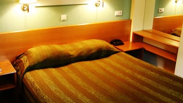 A hotel room with a large bed, two bedside lamps, a framed artwork on the wall, and a mirror above the bed.