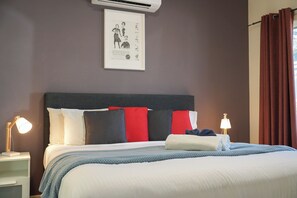 A hotel room with a bed, bedside lamps, a framed artwork on the wall, and a window with curtains. - McLaren Vale Studio Apartments (McLaren Vale)