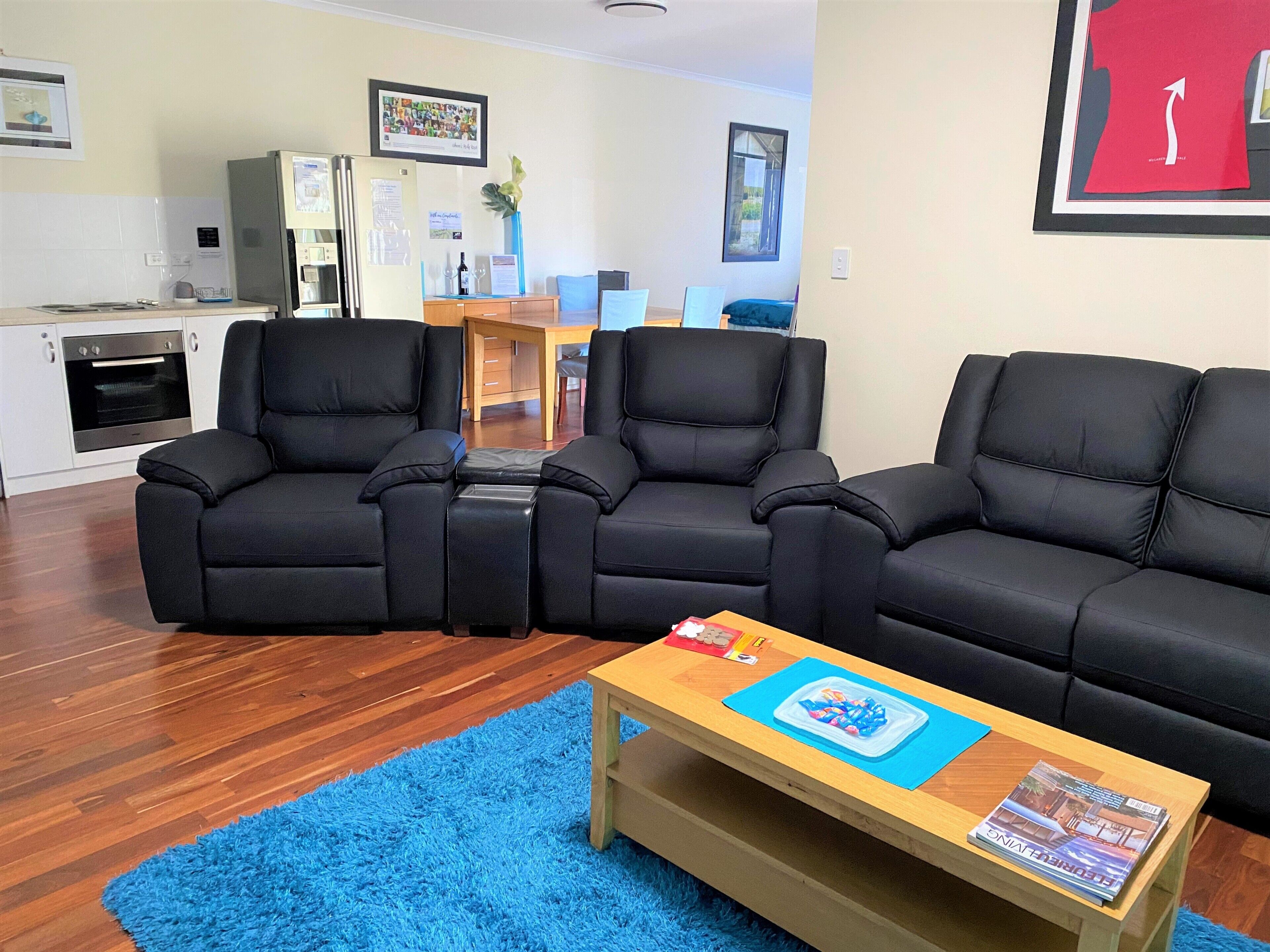 A living room with a black leather sofa, a wooden coffee table, and a blue rug.