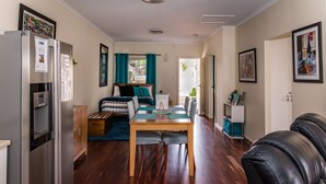 Un espacio habitable compacto con kitchenette, una cama con cortinas color turquesa, una mesa de comedor y un sofá de cuero negro.
