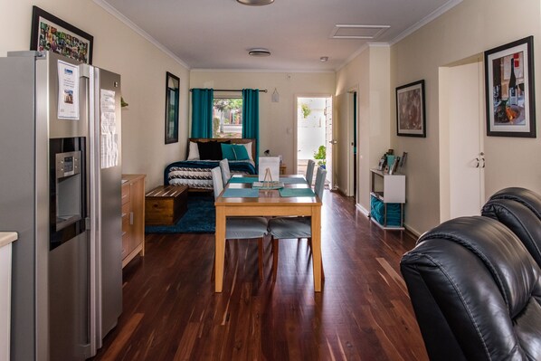 A compact living space with a kitchenette, a bed with teal curtains, a dining table, and a black leather couch.