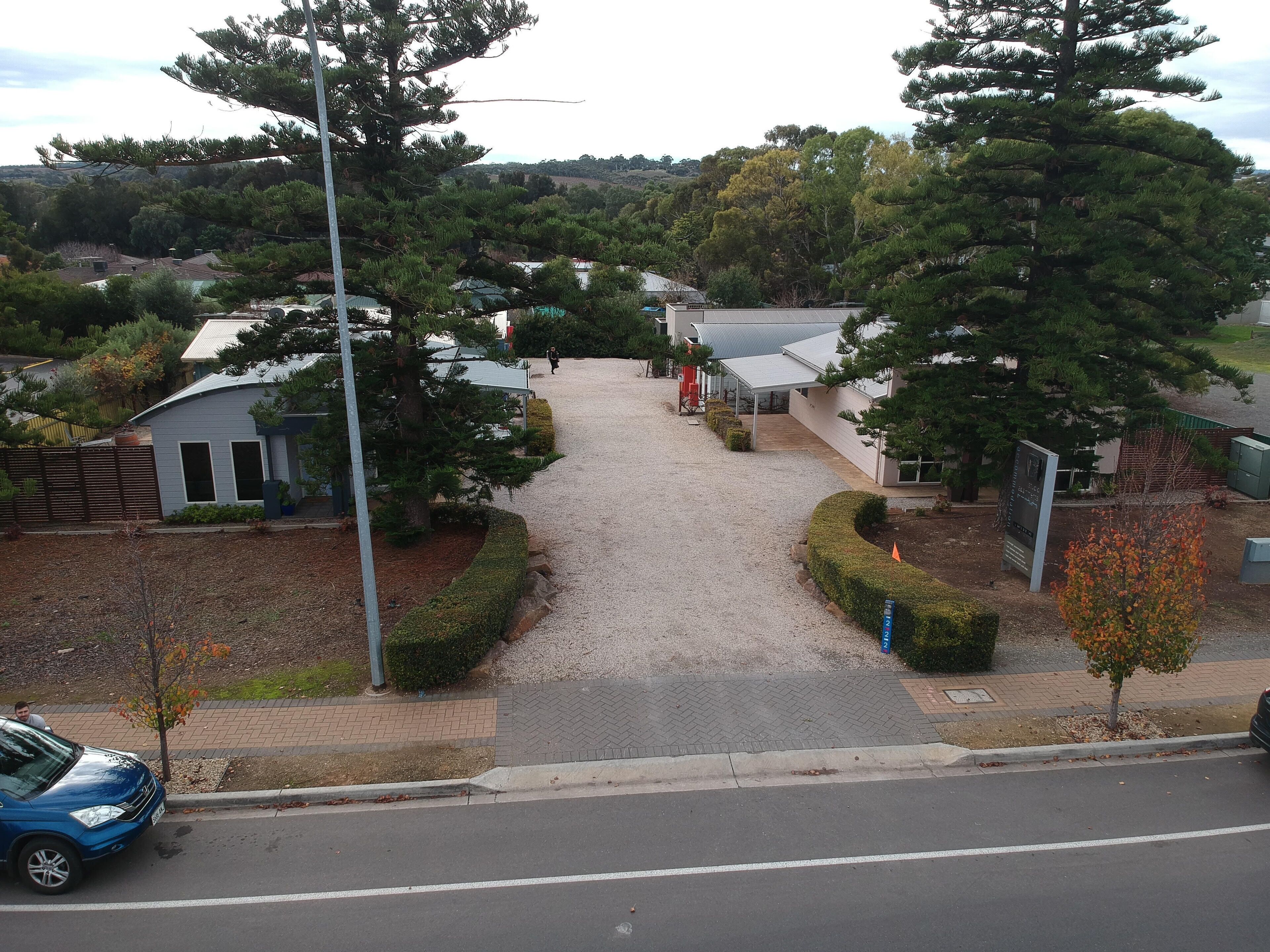 A residential area with houses, a gravel driveway, and a blue car parked on the street.