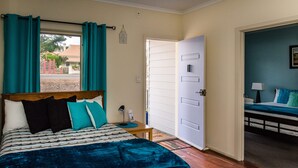 Un dormitorio con cama, mesita de noche, puerta que da a otra habitación y vistas al exterior.