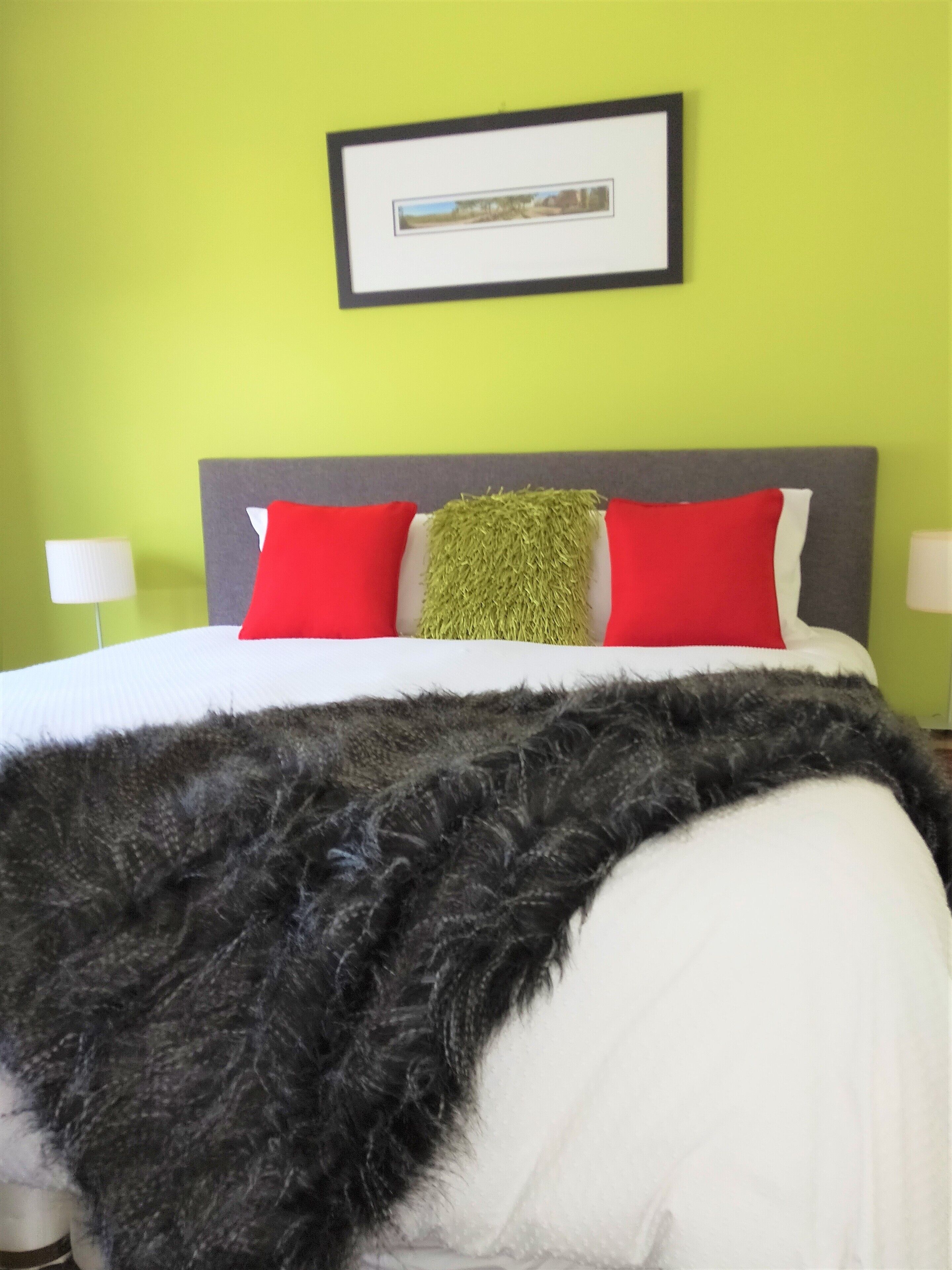 A bed with red and white pillows, a grey headboard, and a framed picture above it.