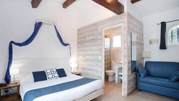 Un dormitorio con cama, mesitas de noche, un sofá azul y un baño visible a través de una puerta abierta.
