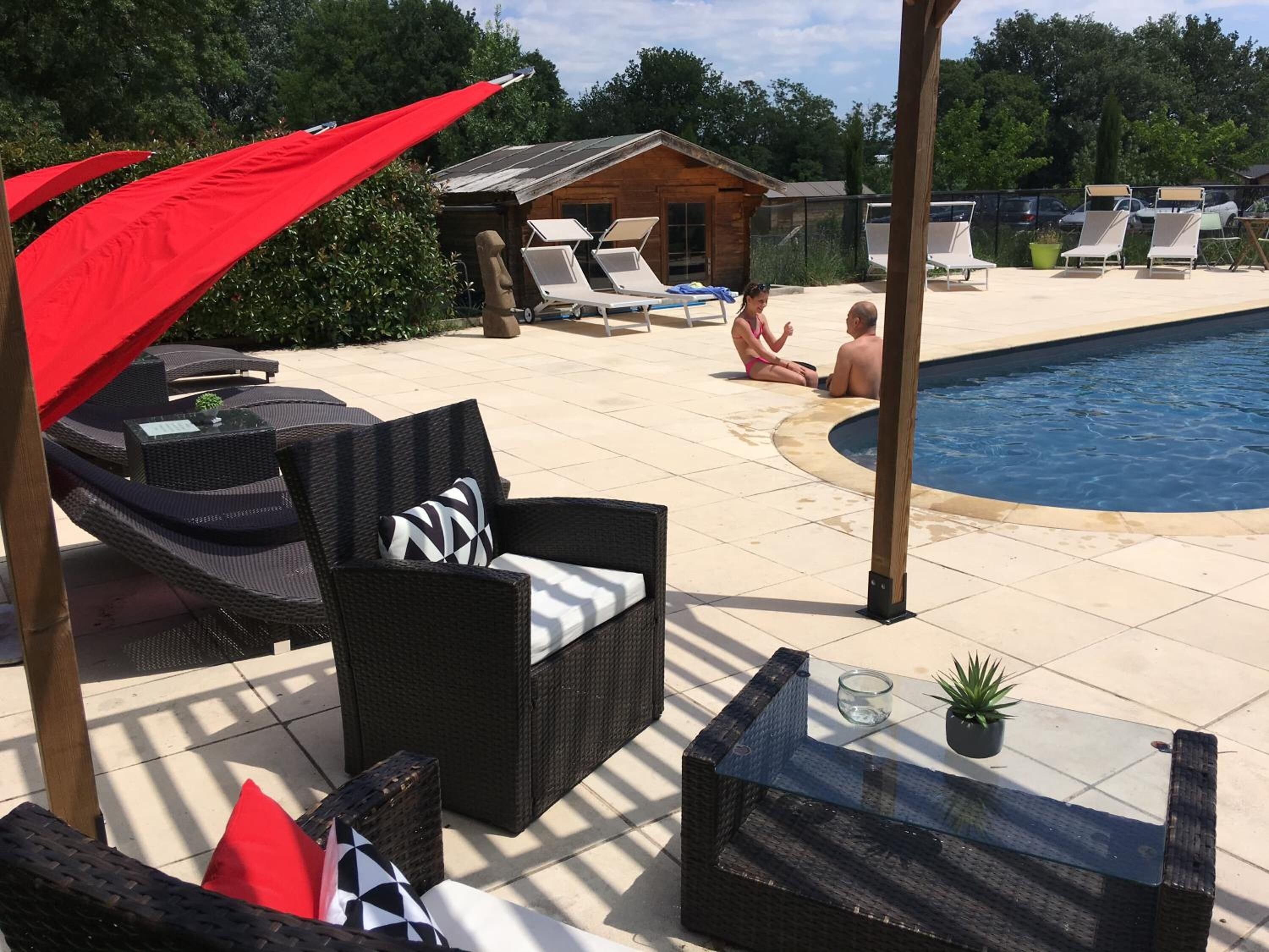 A poolside area with wicker furniture, a glass table, and a red umbrella.