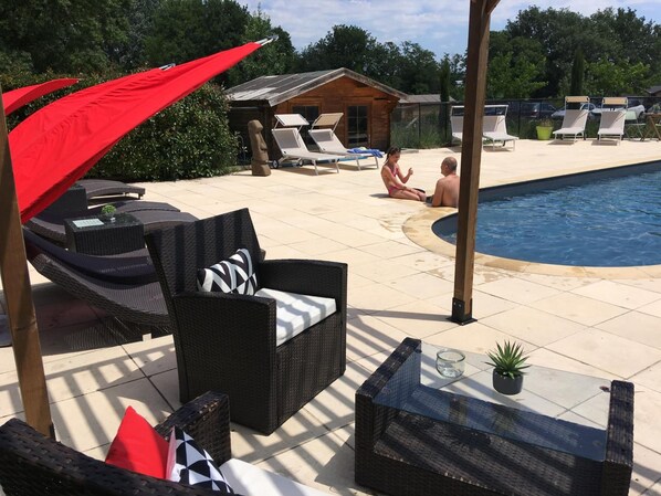 A poolside area with wicker furniture, a glass table, and a red umbrella. - Déjeunez Sous l'Arbre (Rousset)