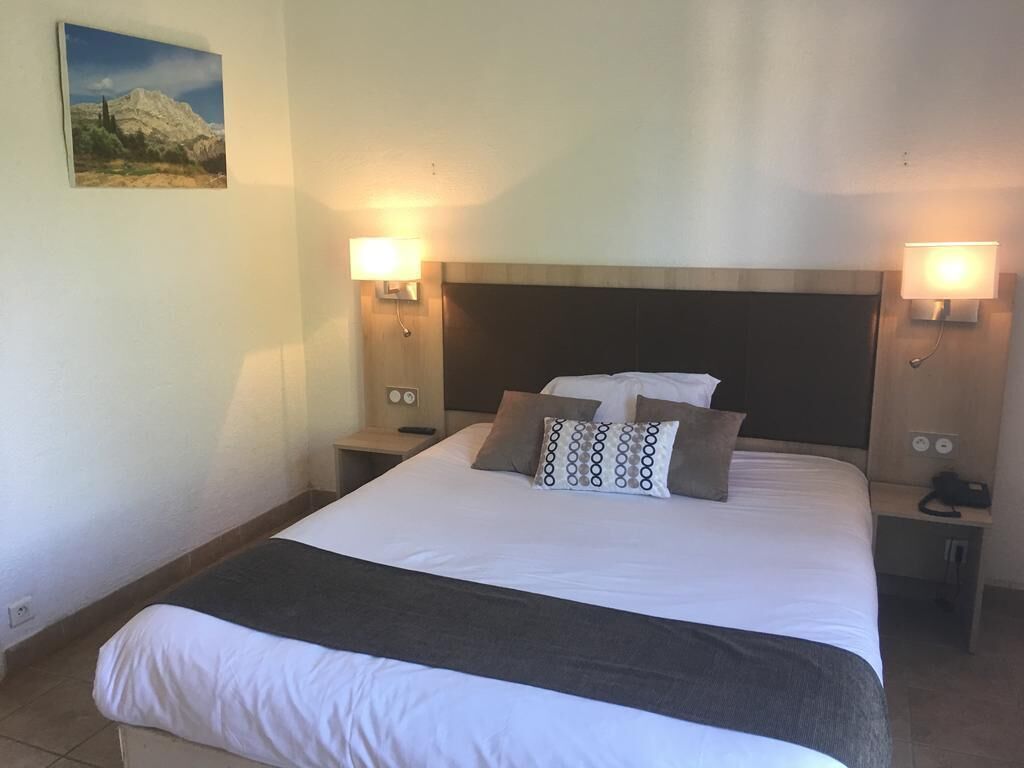 A hotel room with a large bed, two bedside tables, a headboard, and wall-mounted lamps.