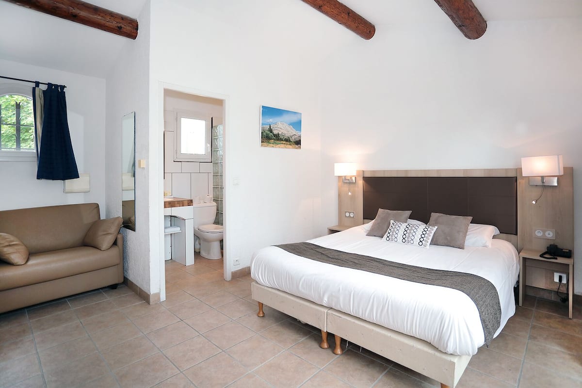 Un dormitorio con cama, mesitas de noche, un tocador, una ventana y un baño con inodoro y lavabo.