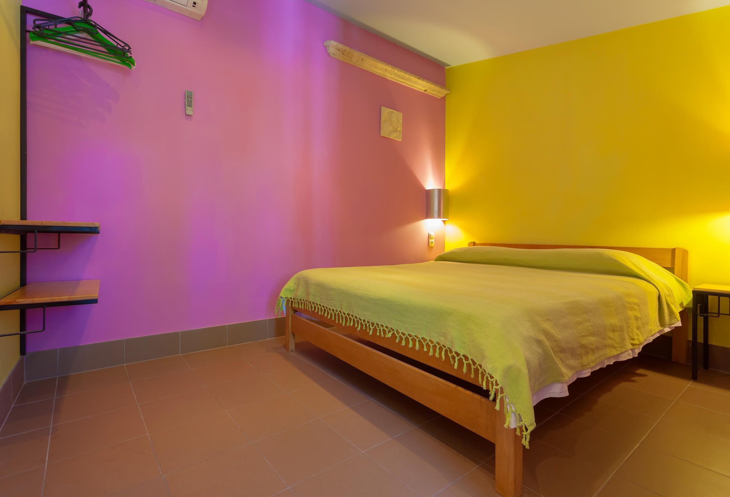 A room with a bed, a shelf, and a wall-mounted lamp.