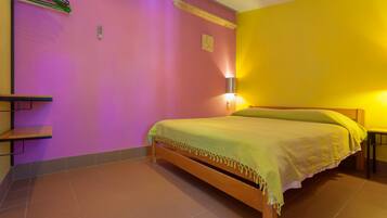 A room with a bed, a shelf, and a wall-mounted lamp.