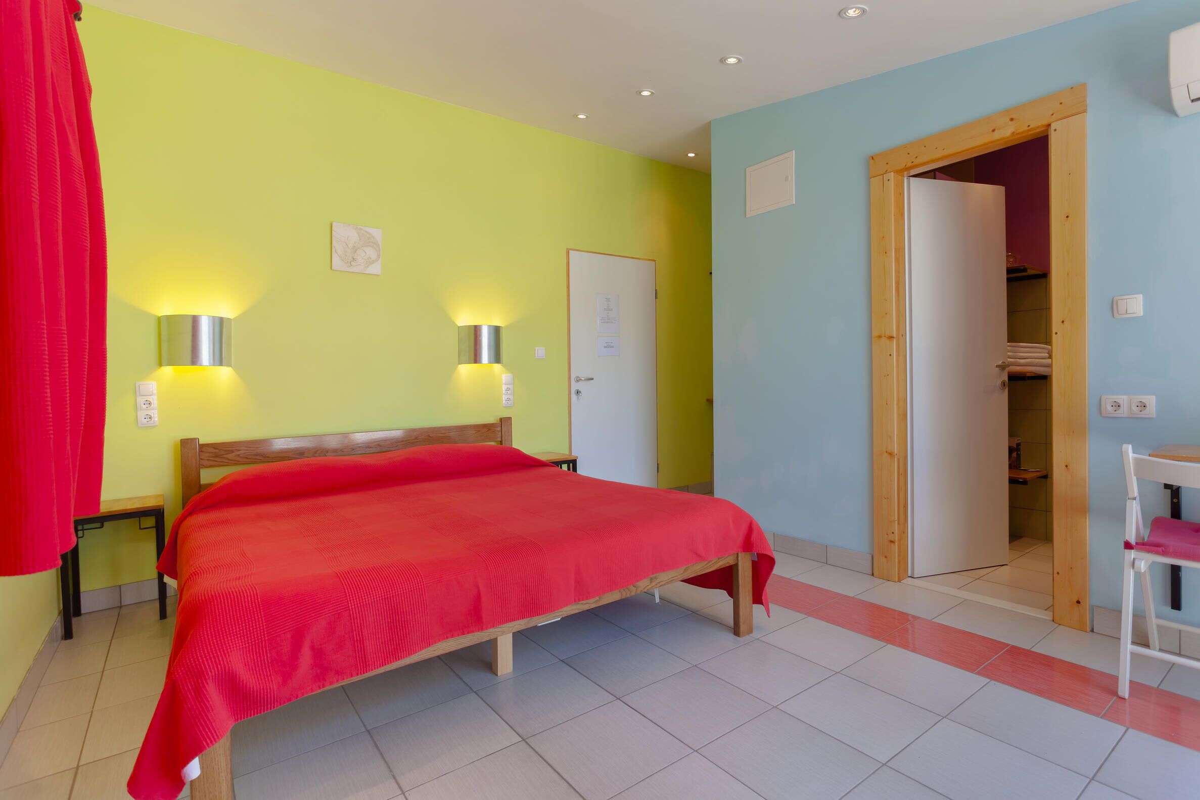 Un dormitorio con una cama, dos lámparas de pared, una puerta y un pequeño banco.