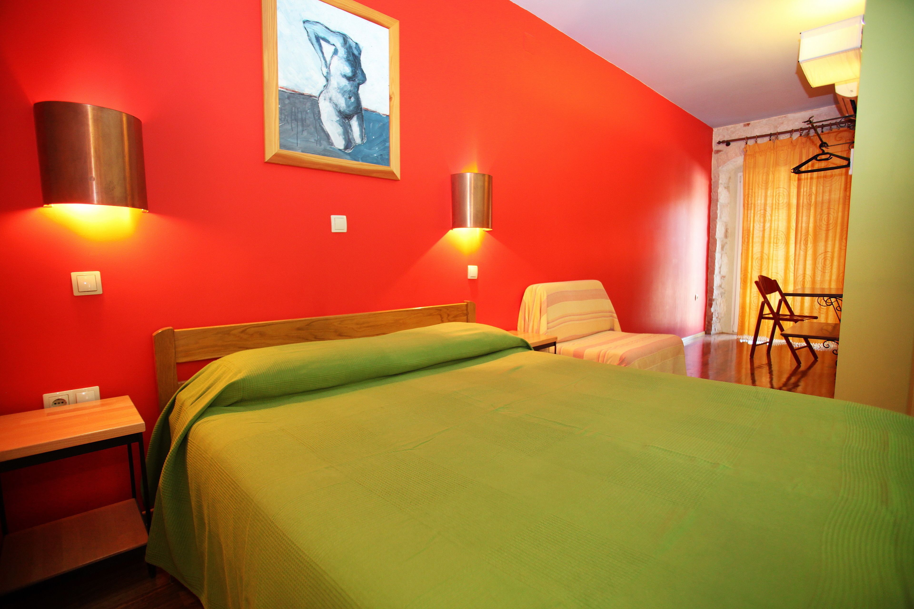 A room with a bed, a chair, a table, and a painting on the wall.